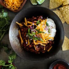 Sweet and Smoky Pineapple Chipotle Chili in a bowl with chips, lime wedges, sour cream and cheese on a table