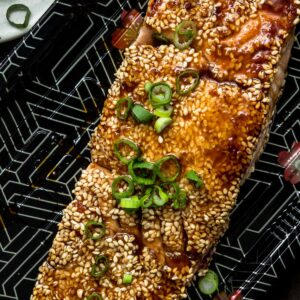 A sesame crusted teriyaki salmon filet on a black takeout tray