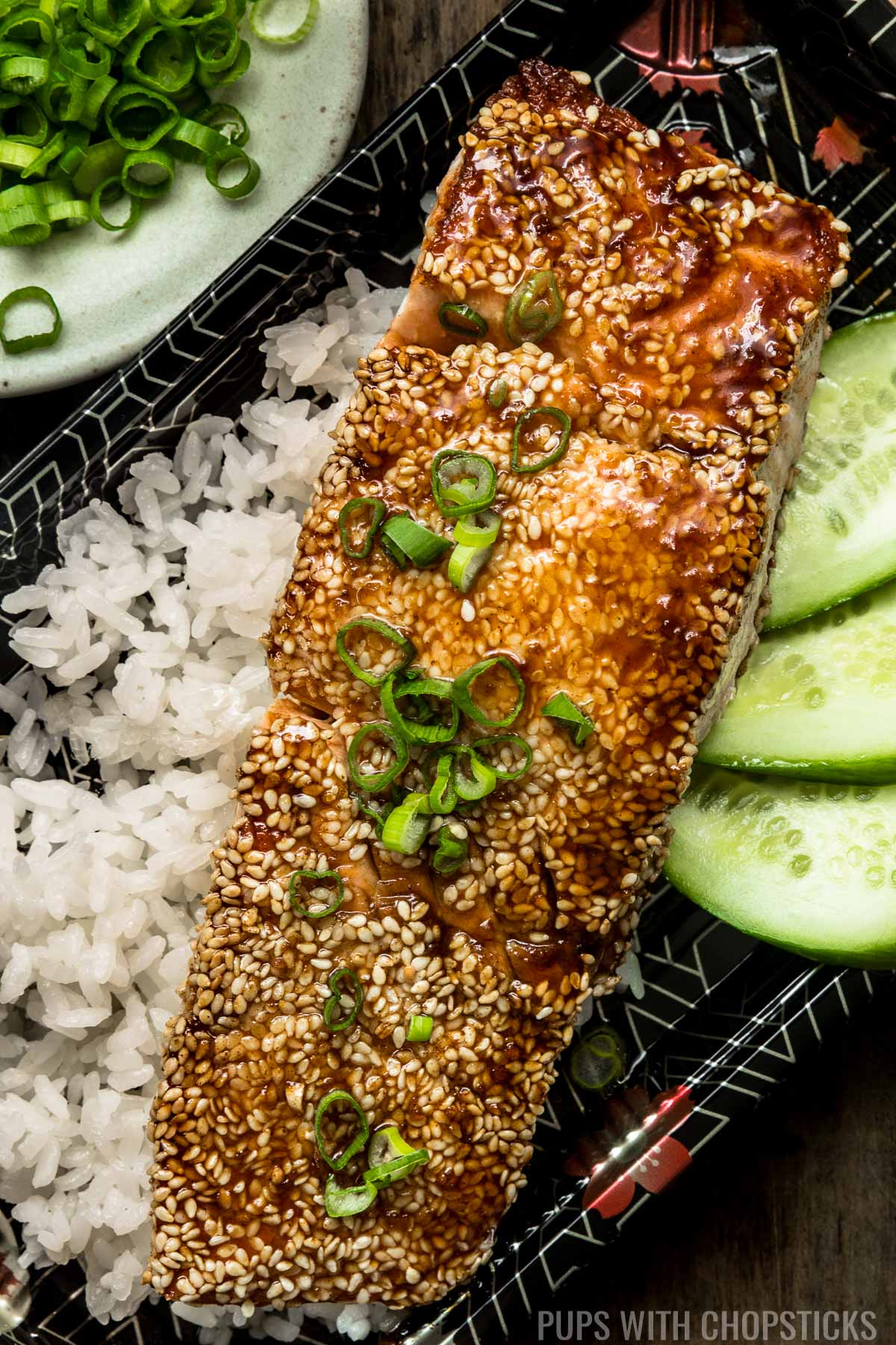 Sesame crusted teriyaki salmon on a bed or rice with a few cucumber slices