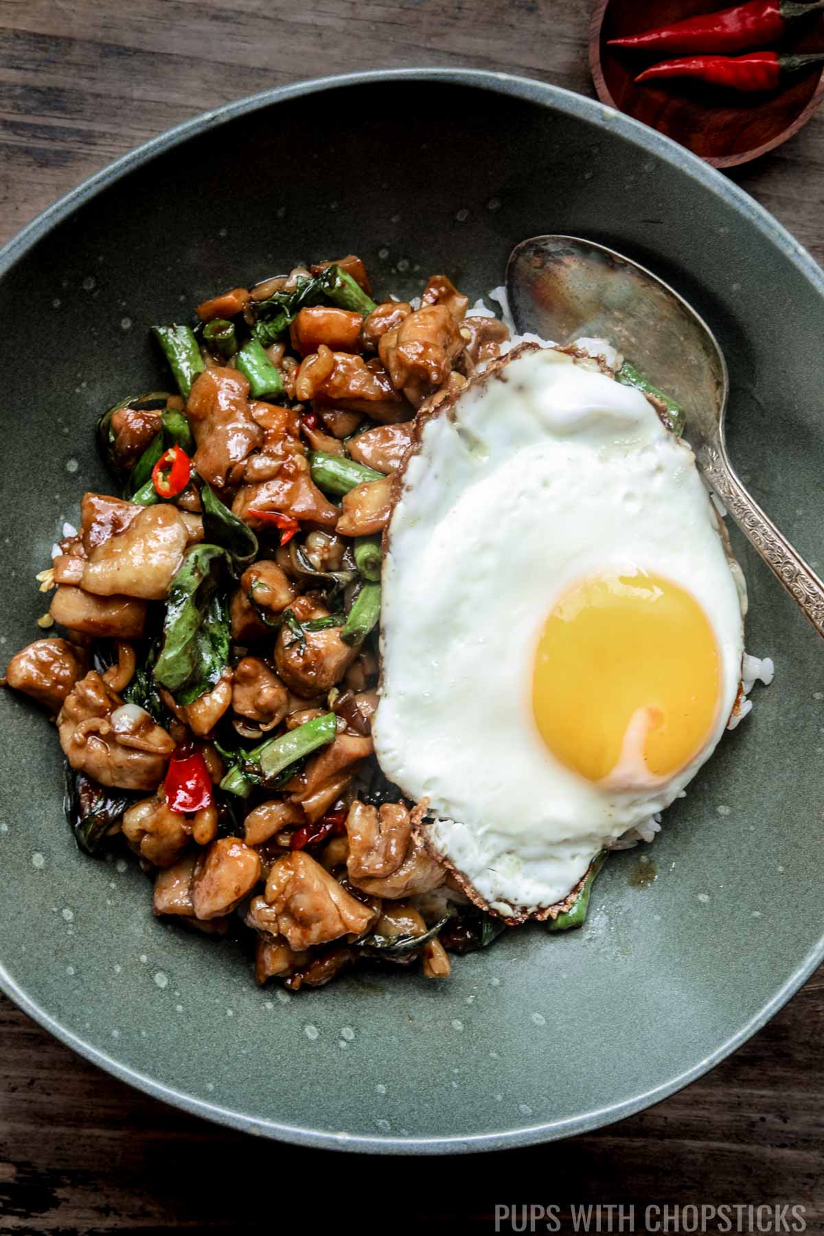 Close up of Thai basil chicken in a green bowl served with white rice and a fried egg