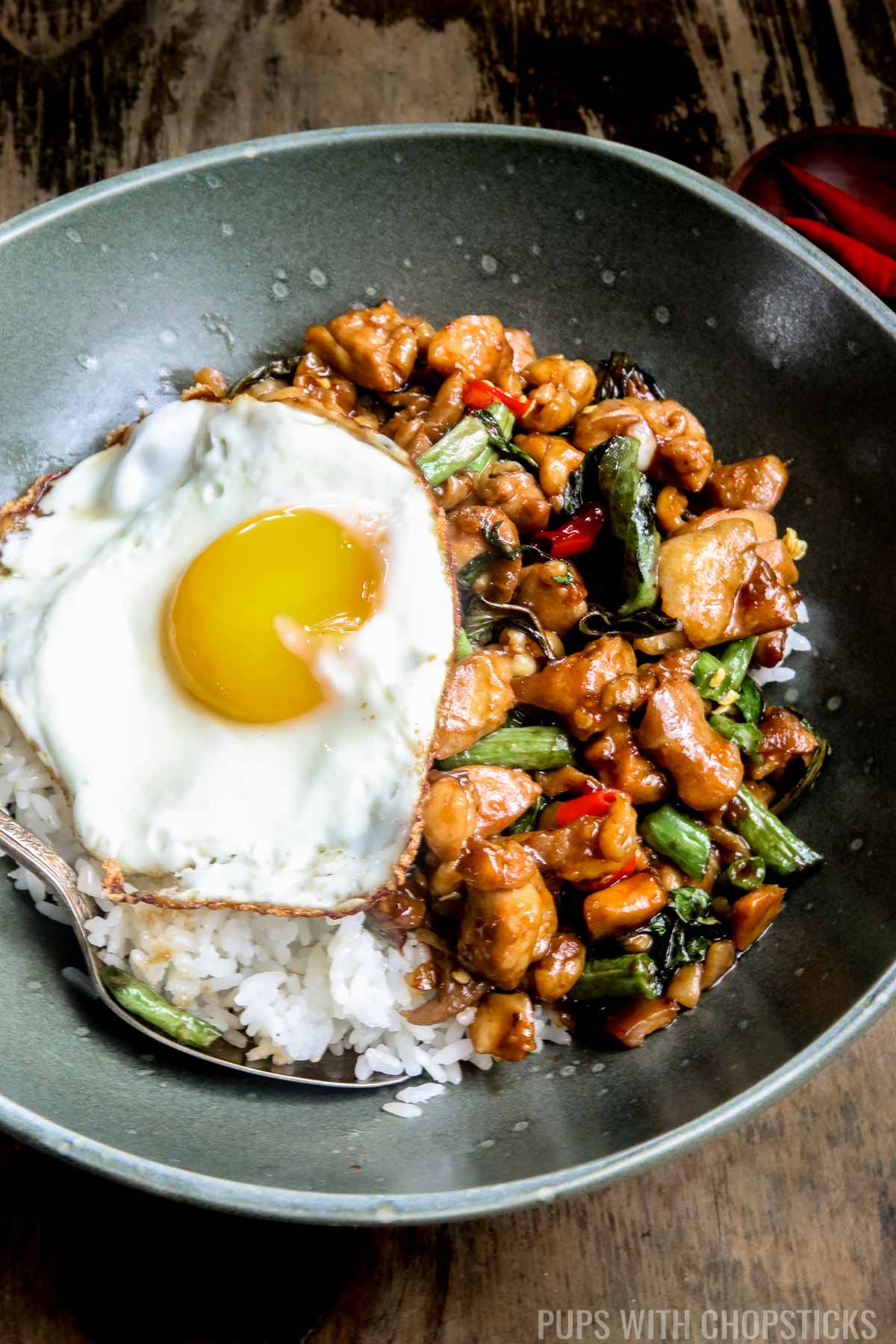 Close up of Thai basil chicken in a green bowl served with white rice and a fried egg