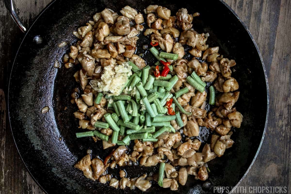 Green beans, red chilies and minced garlic and Thai basil sauce being added to the frying pan to the chicken.