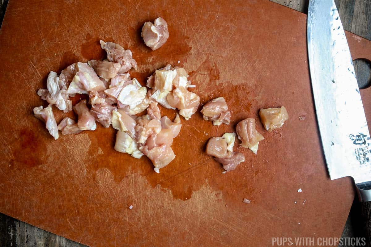 A closeup of raw chicken being diced into small pieces.