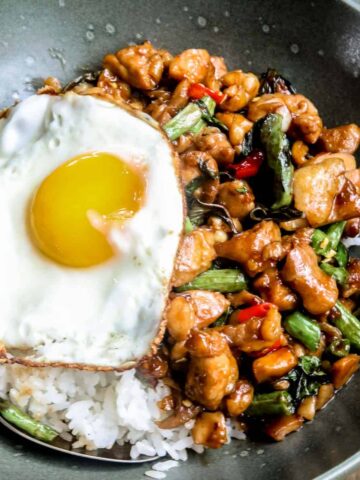 close up of thai basil chicken (pad kaprao) in a green bowl served over rice with a fried egg