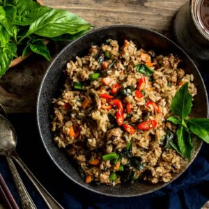 A large bowl of Thai Basil Turkey Fried Rice with a cup of tea on the side and a pair of chopsticks and spoons on the side