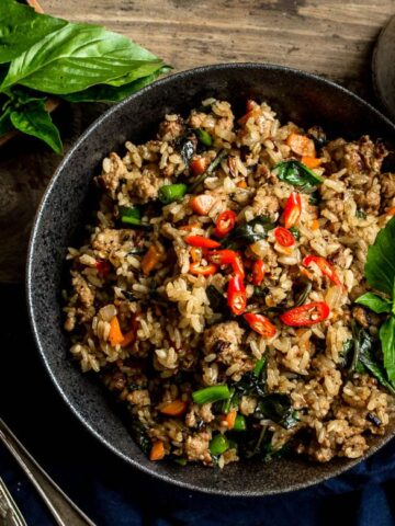 A large bowl of Thai Basil Turkey Fried Rice with a cup of tea on the side and a pair of chopsticks and spoons on the side