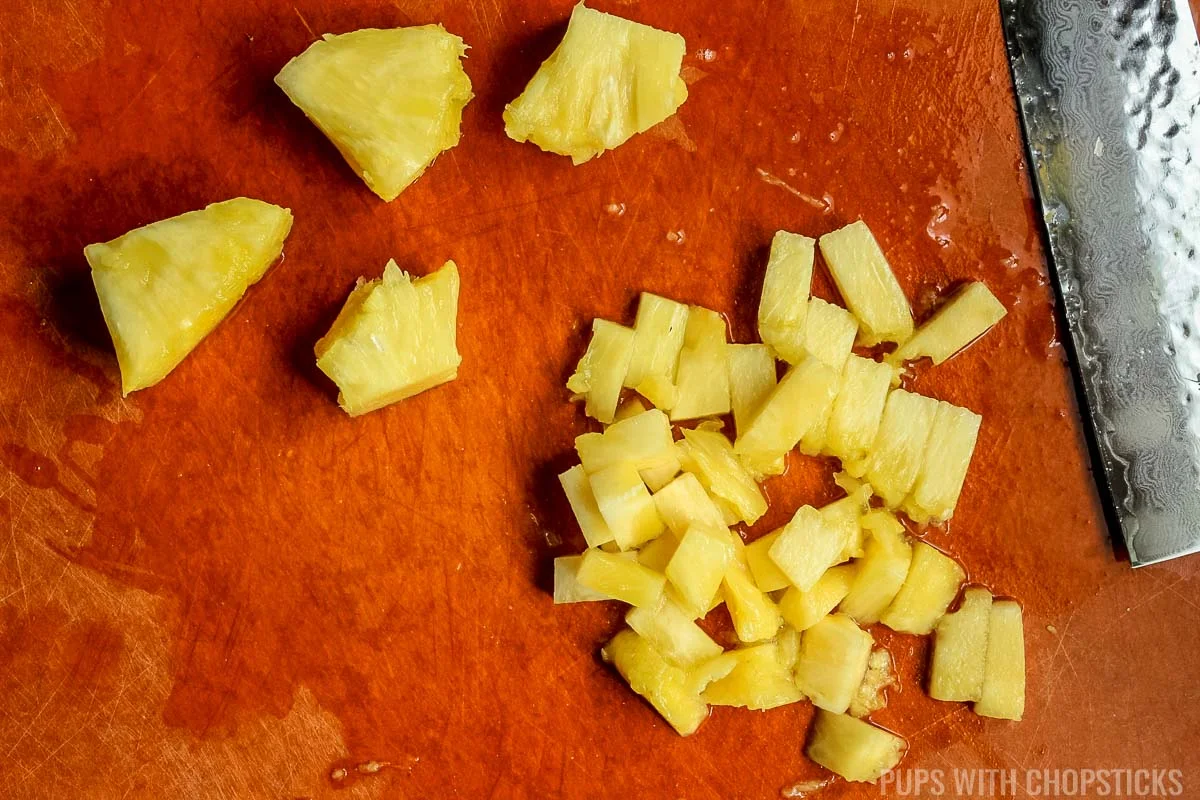 chop pineapple into small pieces on a cutting board.