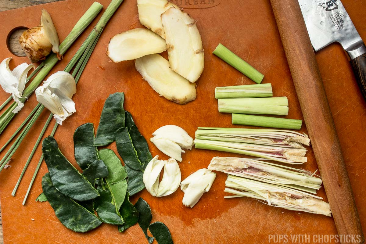 Tom kha gai aromatics (lemongrass, kaffir lime leaves, galangal, garlic) being prepared on a cutting board.