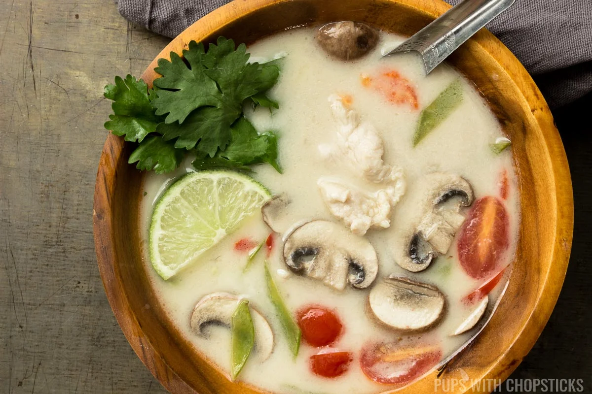 Closeup of tom kha soup in a wooden bowl with a metal spoon