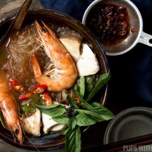 A bowl of tom yum goong soup with shrimp and glass noodles served with a side of chilli oil