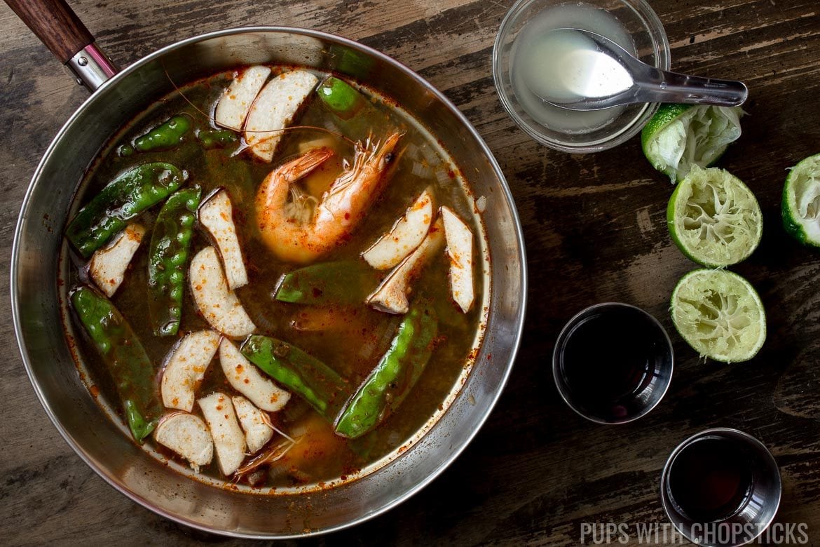 Tom Yum Goong in a large pot with no heat being seasoned with fish sauce and fresh lime juice