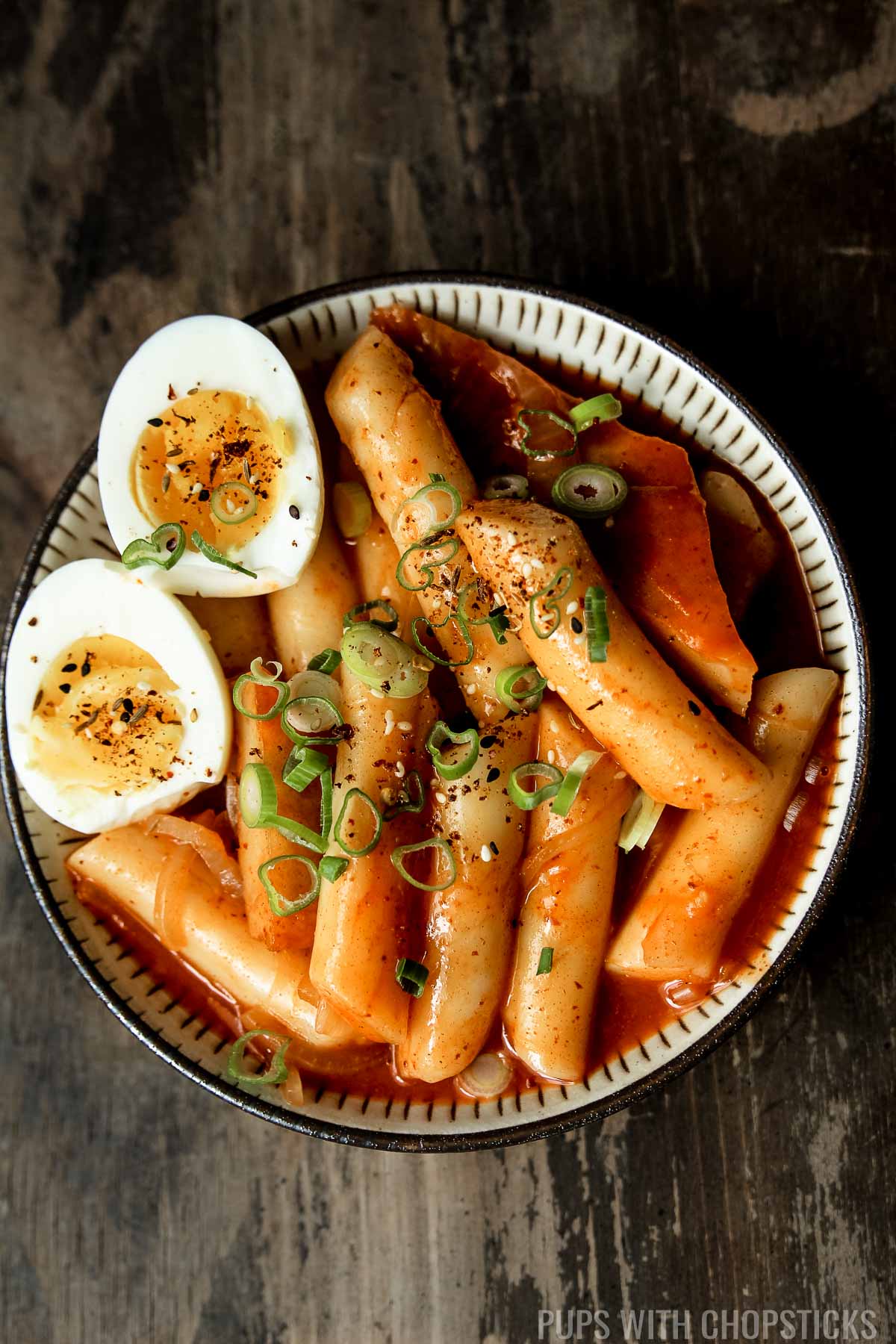 A small bowl of tteokbokki (Spicy korean rice cakes) with medium boiled eggs sliced in half and garnished with green onions
