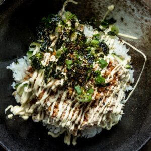 A close up of a bowl of tuna mayo rice bowl (deopbap) with green onions and roasted seaweed on top, drizzled with mayo