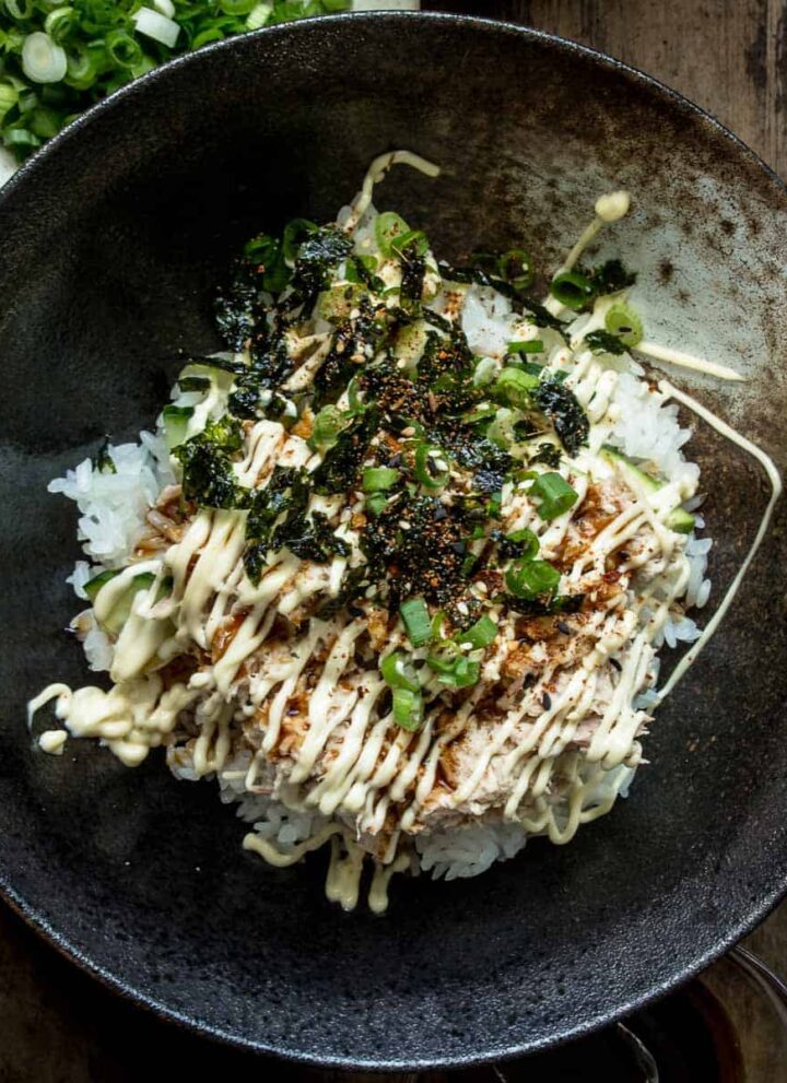 A close up of a bowl of tuna mayo rice bowl (deopbap) with green onions and roasted seaweed on top, drizzled with mayo