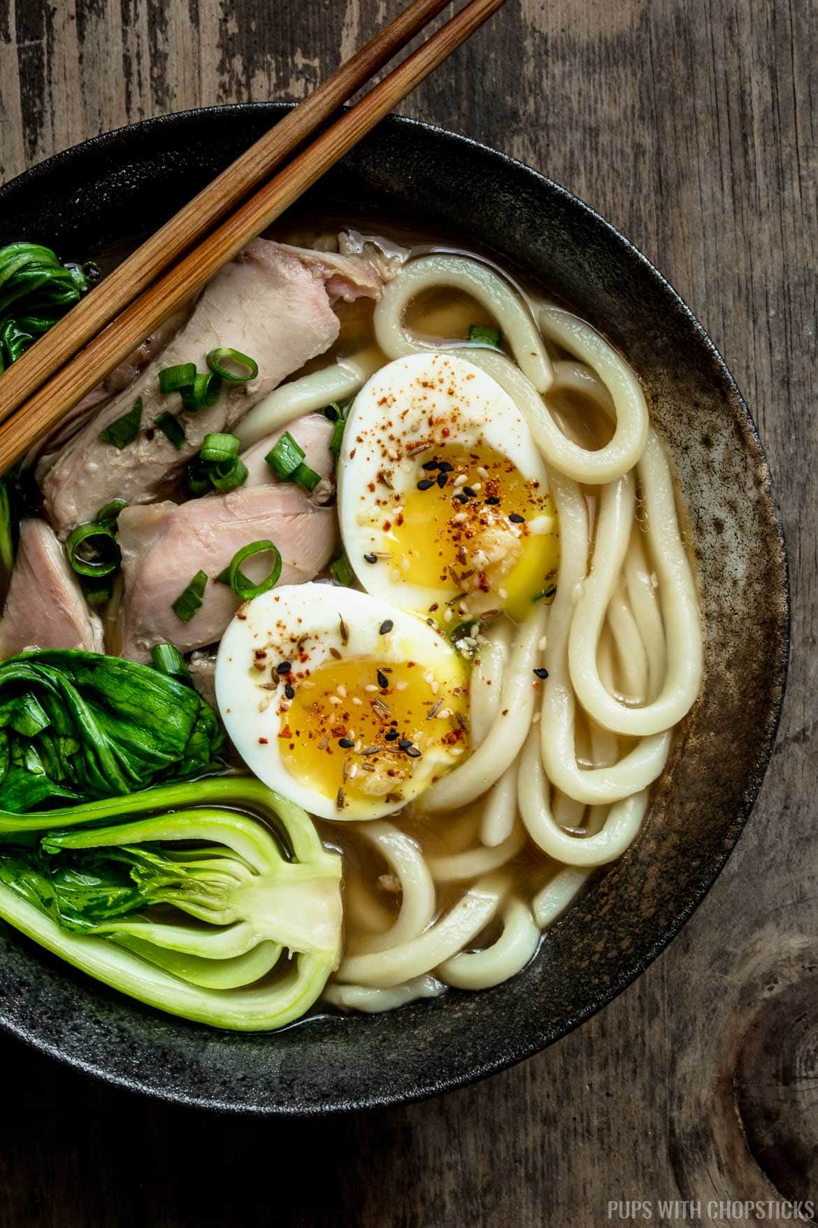 A large bowl of turkey udon noodle soup with soft boil egg, leftover turkey and bok choy on top