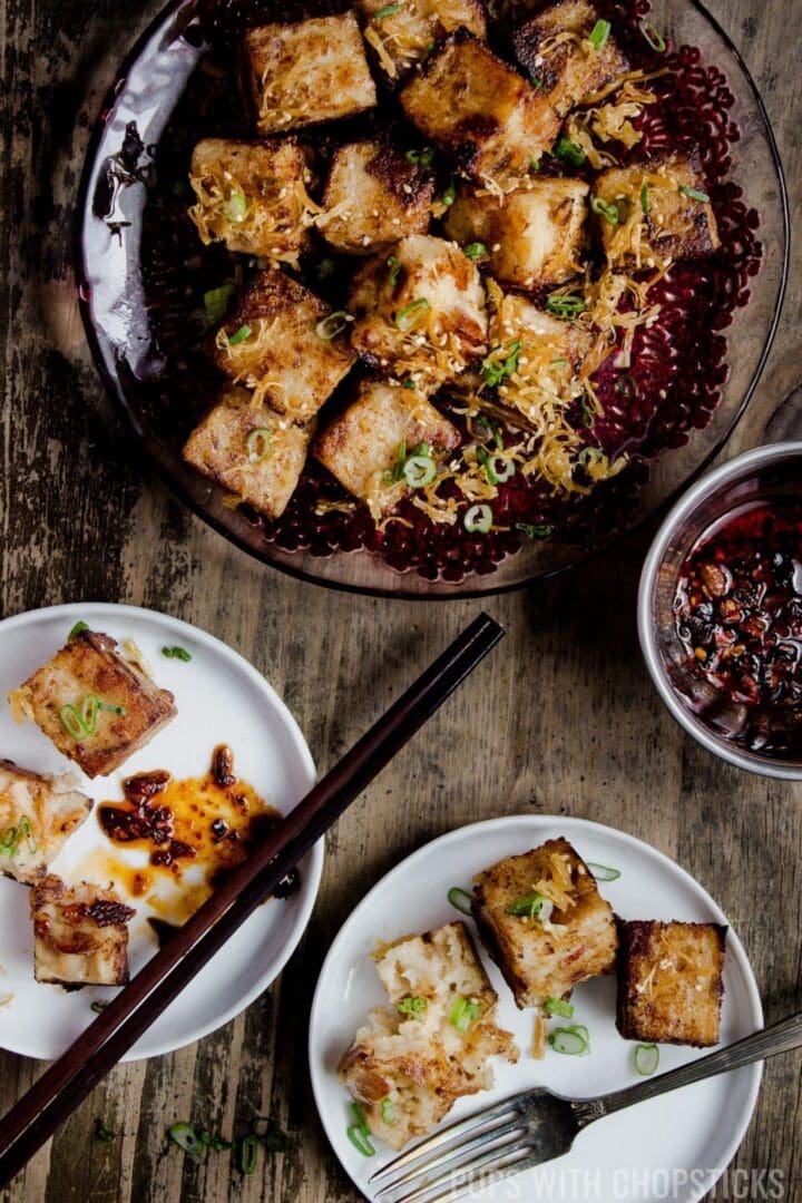 A plate of chinese turnip cake served with a side of chili oil with 2 plates being served on