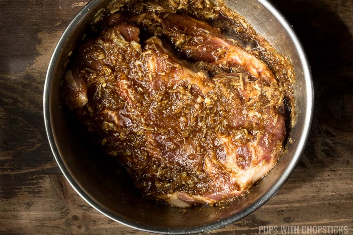 A large bowl of pork shoulder with the lemongrass marinade slathered on it in a metal bowl.