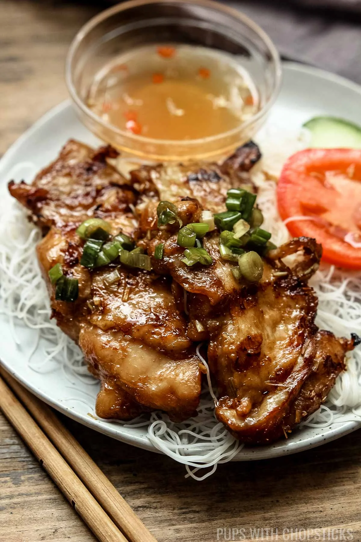 A close up of lemongrass chicken being served with vermicelli rice noodles on a white plate with a side of nuoc cham.