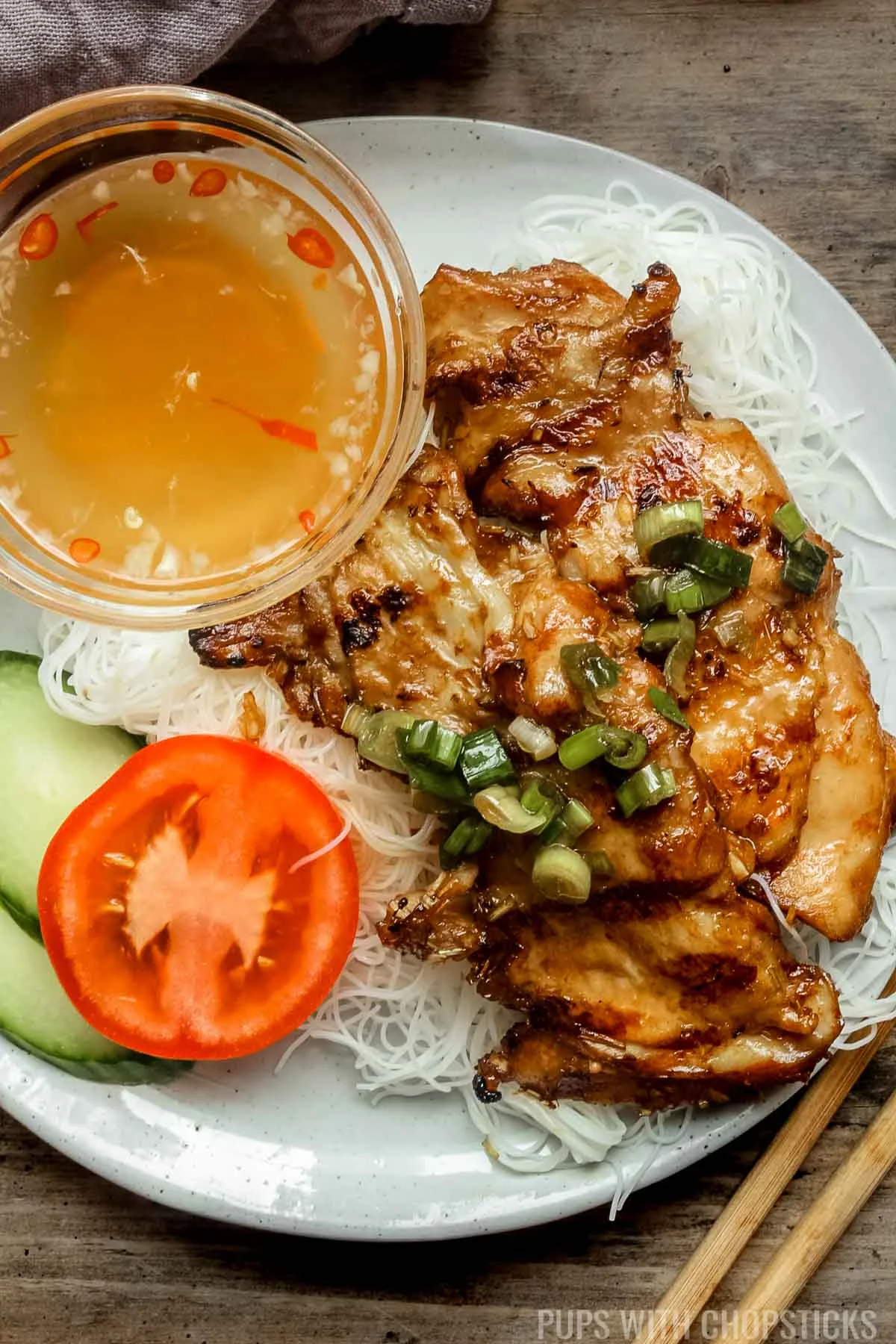 A top view of Vietnamese lemongrass chicken served with vermicelli rice noodles on a white plate with a grey napkin.