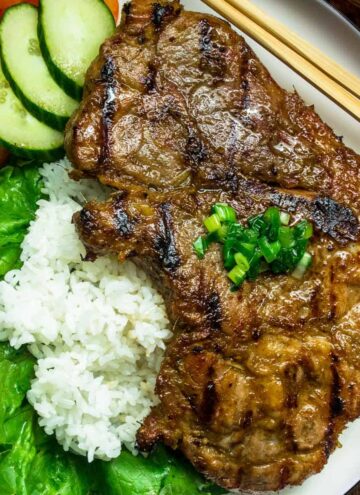Vietnamese lemongrass pork chops served on a large white plate with rice, tomatoes and cucumber with a side of nuoc cham dipping sauce