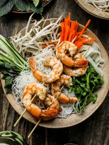 A bowl of Vietnamese vermicelli noodles with shrimp on top served with fresh vegetables