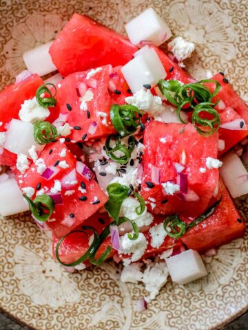 Closeup of watermelon feta salad served in a beige bowl with green onions on top.