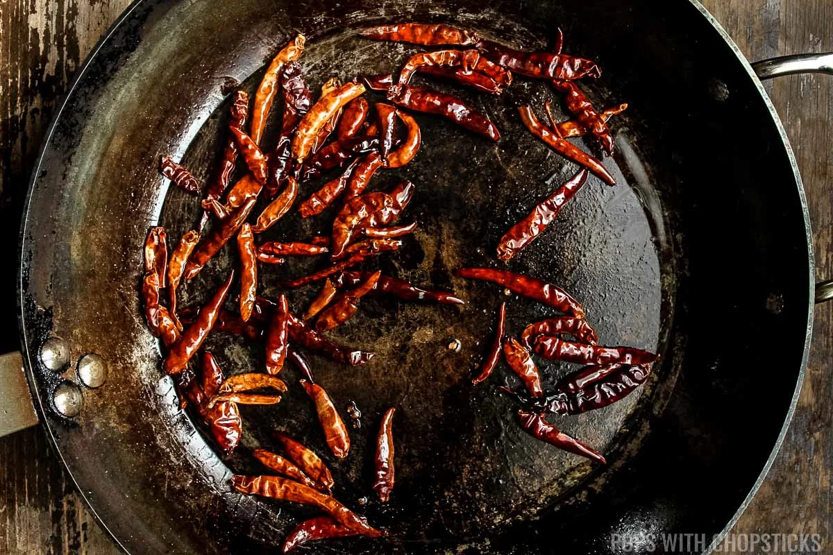 dried red chili peppers being stir fried in frying pan.