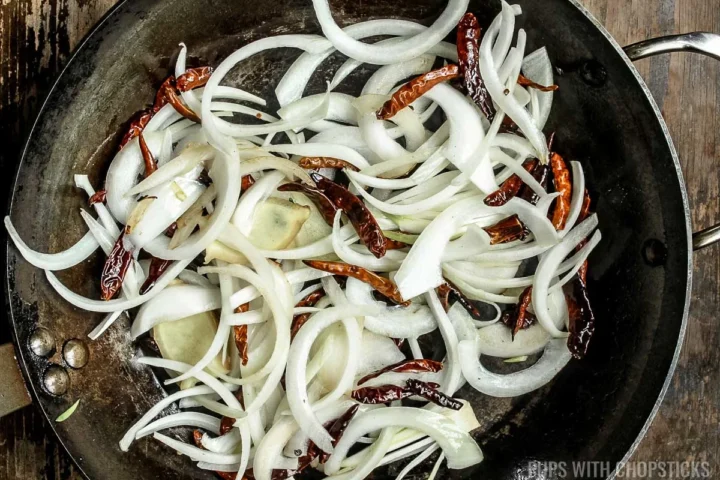 add onions and aromatics to frying pan and stir with dried chilis.