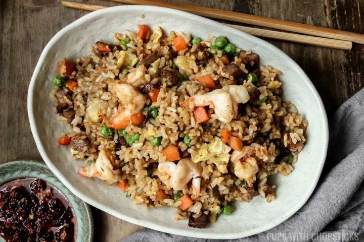 yeung chow fried rice in a white bowl with wooden chopsticks and grey napkin.