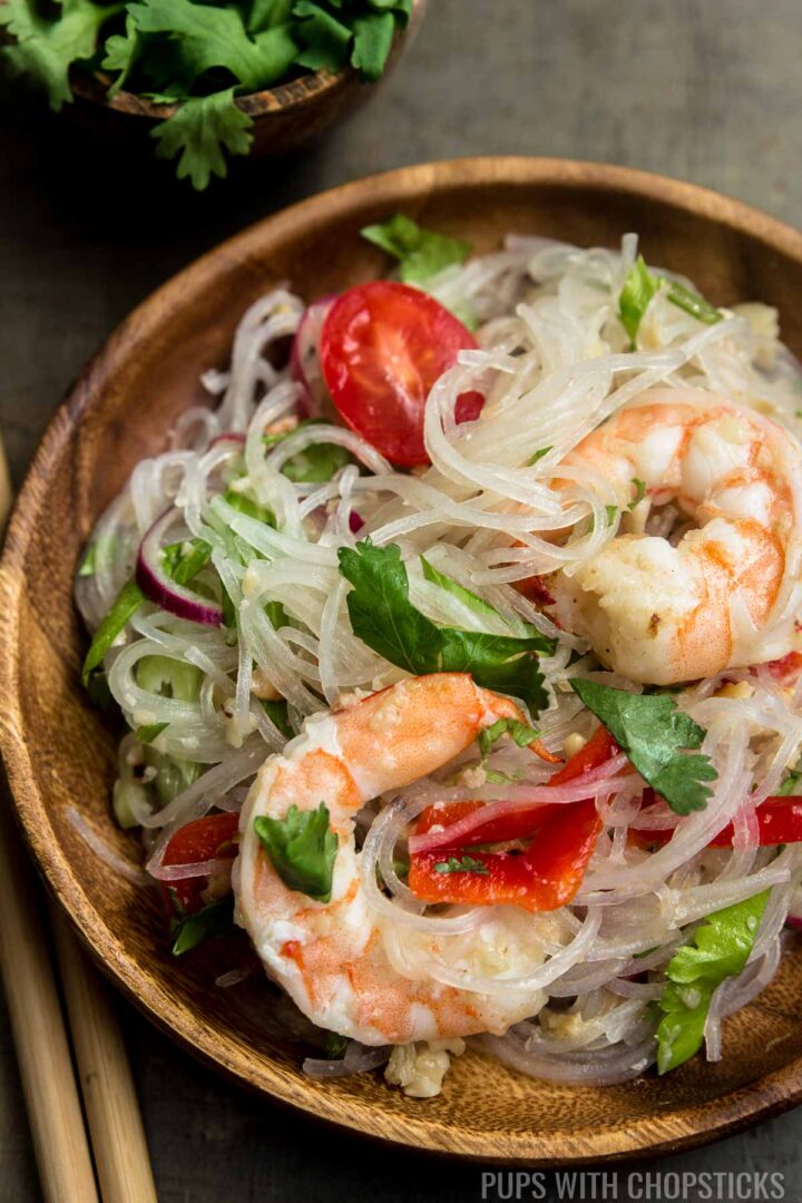 Thai glass noodle salad (yum woon sen) on a wooden plate with shrimp on top